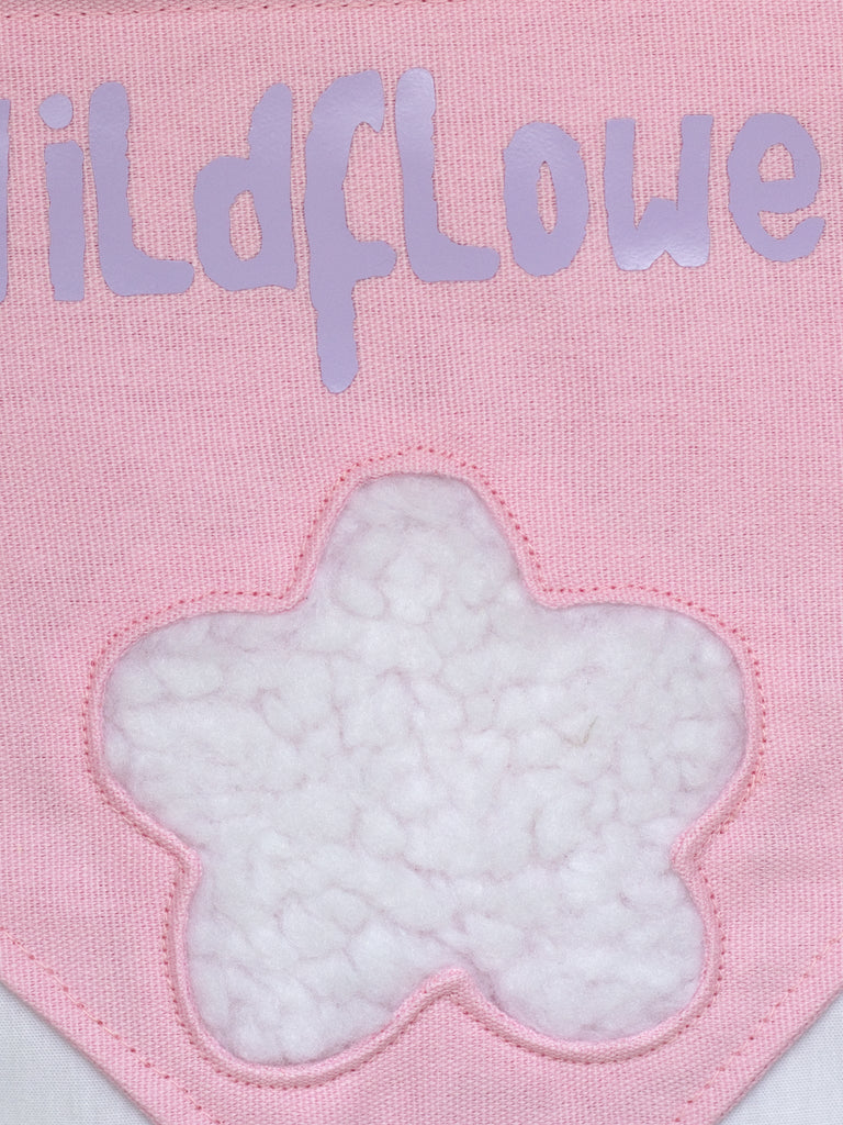 A close-up of a pink canvas banner that reads Wildflower with a fluffy white flower.