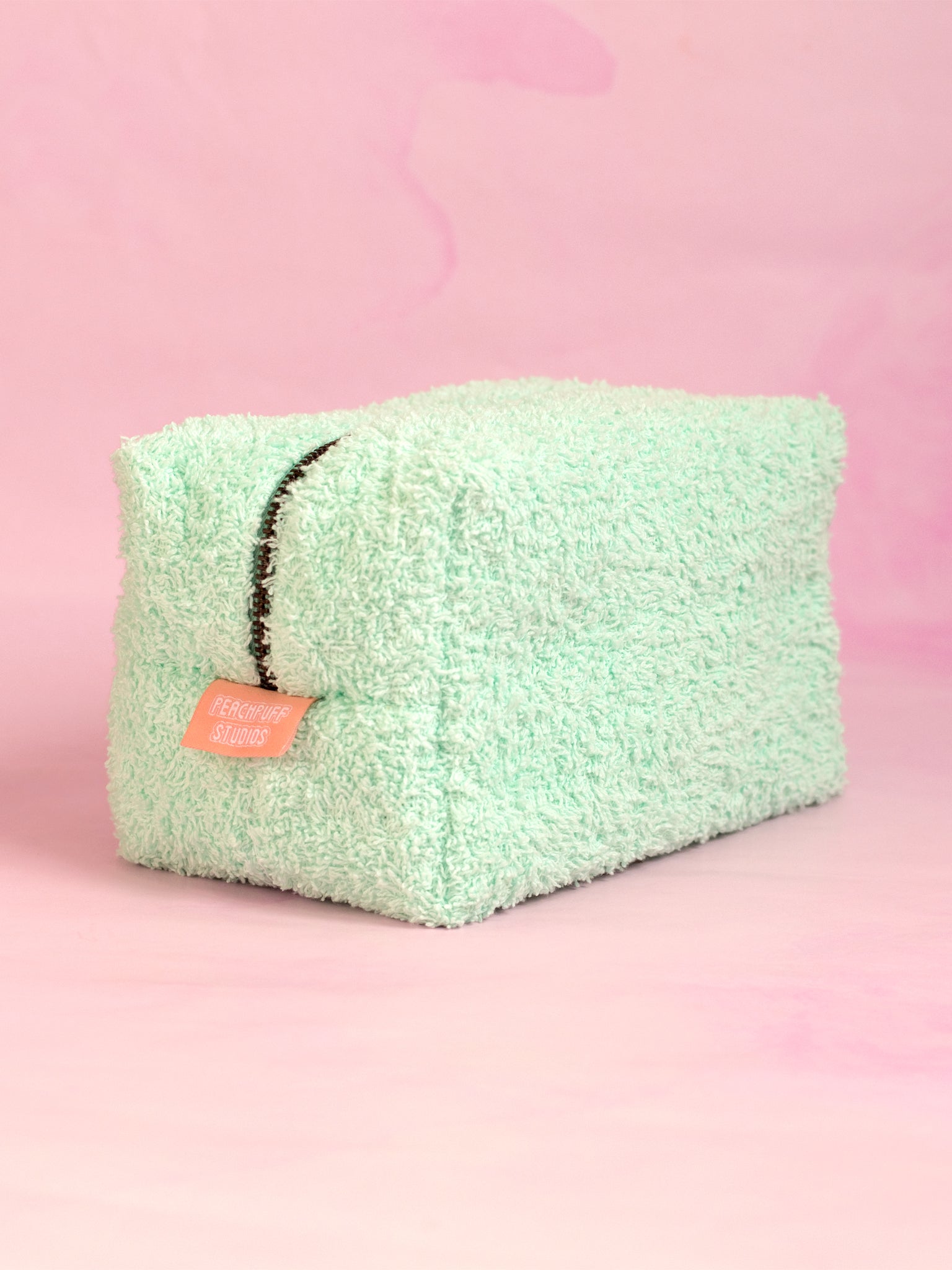 A mint green towelling makeup bag on a pink marbled foreground.