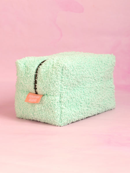 A mint green towelling makeup bag on a pink marbled foreground.