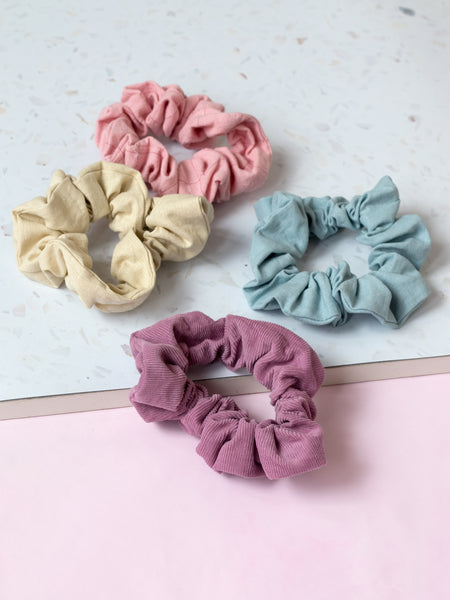 Four different coloured pastel scrunchies are placed next to each other on a terrazzo and pink tabletop.