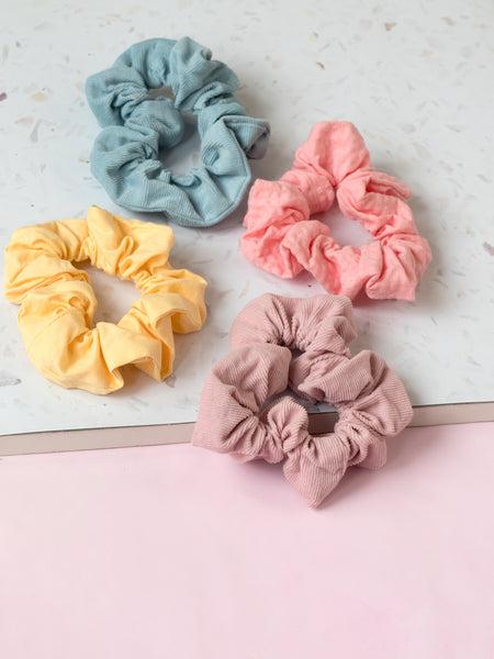 Four different coloured pastel scrunchies are placed next to each other on a terrazzo and pink tabletop. 