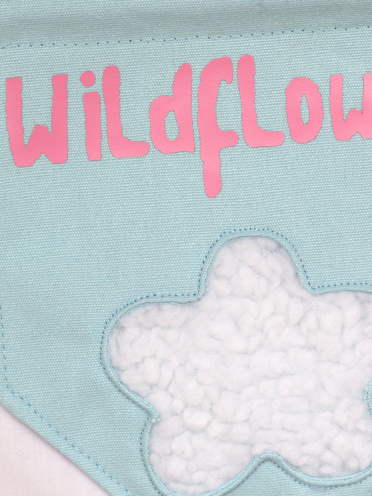 A close-up of a blue canvas banner that reads Wildflower with a fluffy white flower.