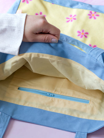 A female hand opens a tote bag to reveal an inside zipper pocket.