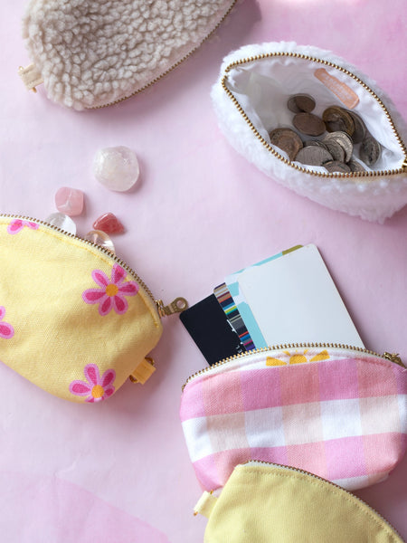 A group of five different coloured coin purses on a pink-marbled floor. One of the purses is open with change, another with crystals falling out, and another with cards.