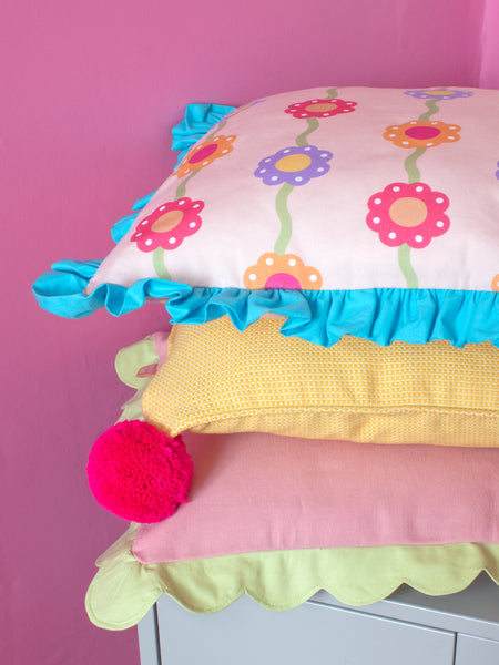 Three different colourful cushions are placed on top of each other on a grey cabinet in a pink room.