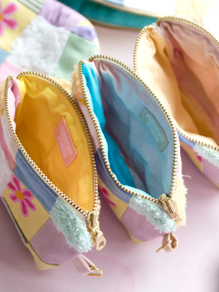 A group of three multi-coloured patchwork coin purses open on a pink table to show the different coloured linings.