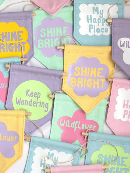 A group of colourful wall banners with different affirmations are laid on top of one another.