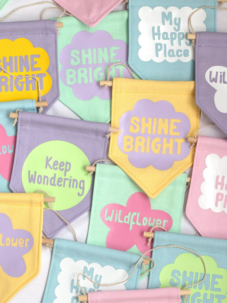 A group of colourful wall banners with different affirmations are laid on top of one another.