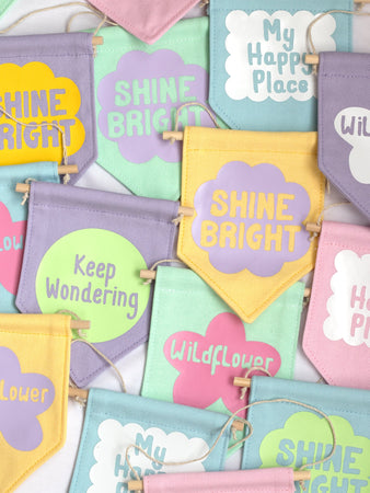A group of colourful wall banners with different affirmations are laid on top of one another.