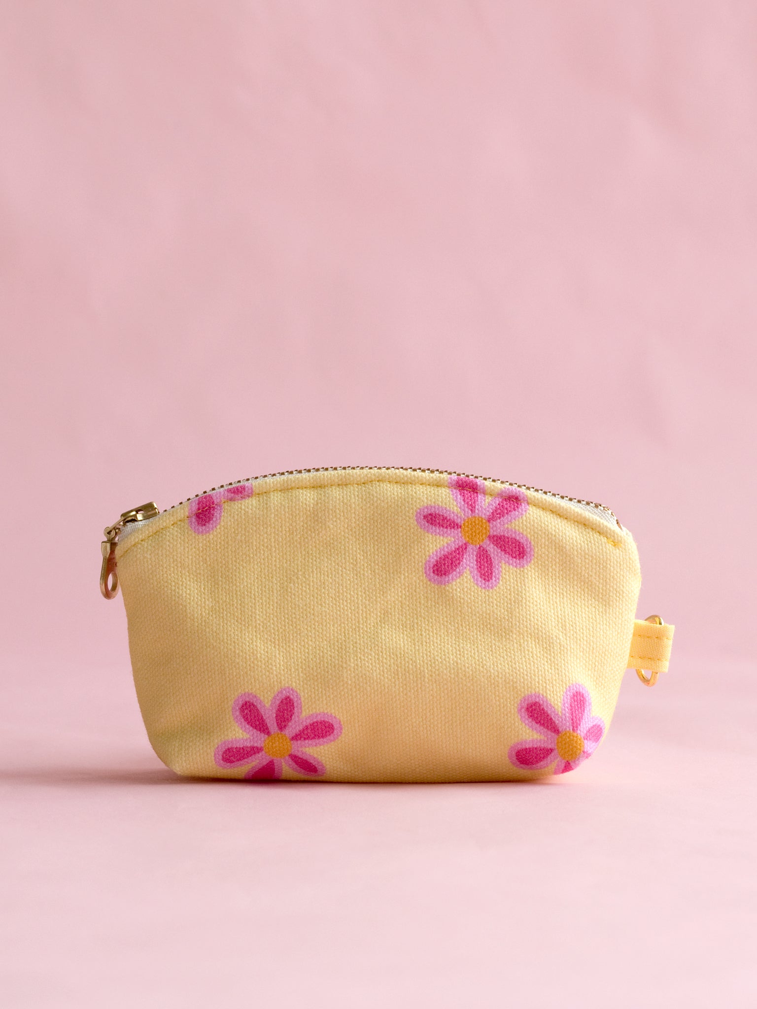 A yellow floral coin purse with a metal zip and ring hook on a pink foreground.