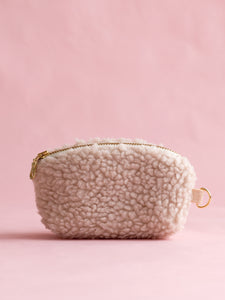 A cream fluffy coin purse with a metal zip and ring hook on a pink foreground.