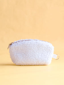 A white fluffy coin purse with a metal zip and ring hook on a yellow foreground.