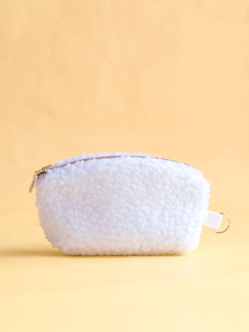 A white fluffy coin purse with a metal zip and ring hook on a yellow foreground.