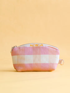 A pink gingham and yellow sunshine printed coin purse with a metal zip and ring hook on a yellow foreground.