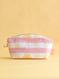 A curved top zip pouched in a pink gingham printed fabric on a yellow foreground.