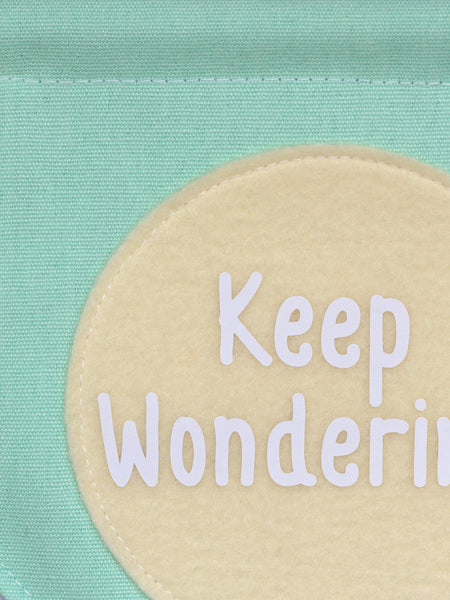 A close-up of a green canvas banner that reads 'Keep Wondering' in a yellow circle.
