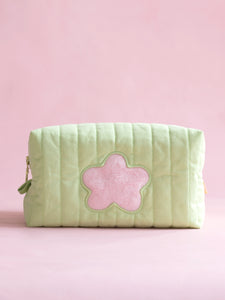 A green quilted makeup bag with a fluffy pink flower in the centre on a pink foreground.