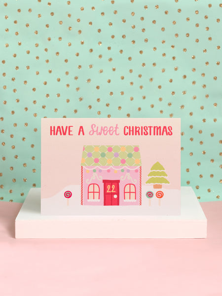 A Christmaa card with a pastel candy house and 'Have A Sweet Christmas' written on top on a white block.