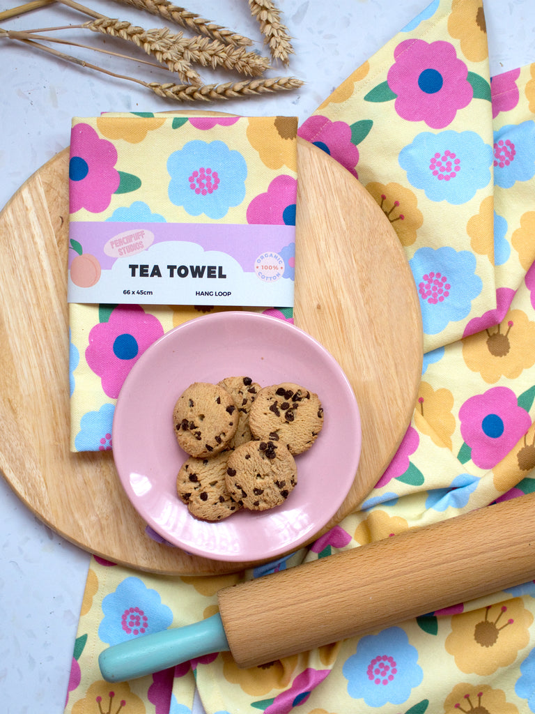 a kitchen flat lay with a yellow floral tea towel, cookies and a rolling pin