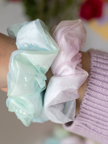 A close-up of two rainbow-coloured scrunchies that are on a female wrist.