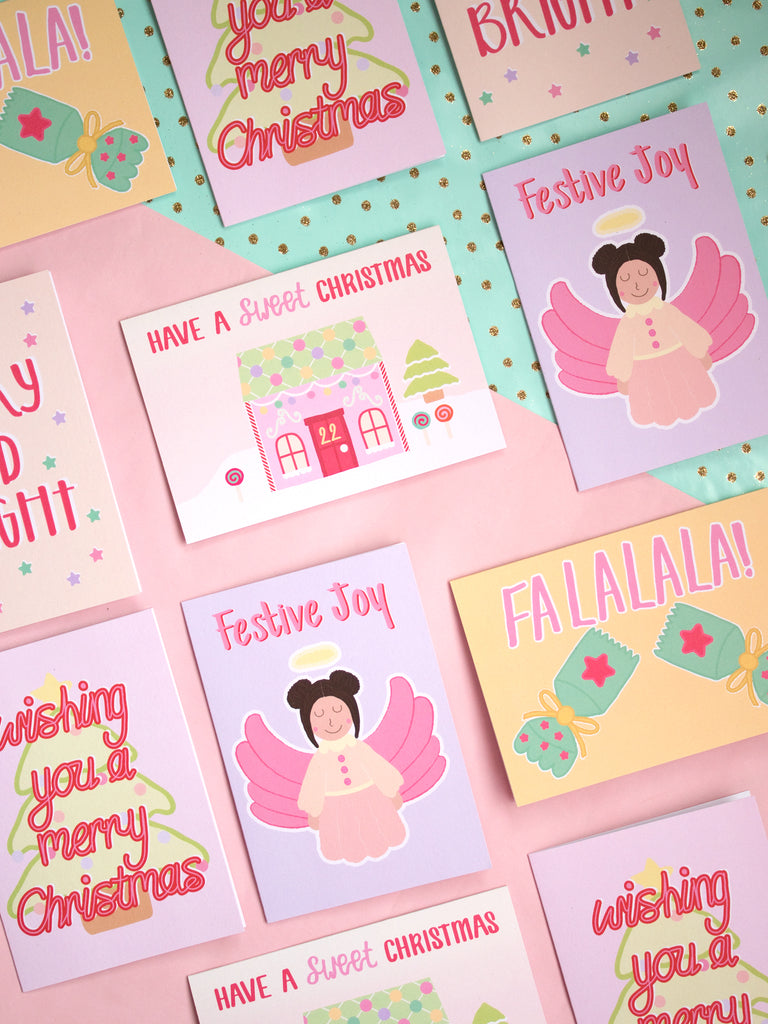 A selection of fun and pastel Christmas cards lay on a pink and turquoise background.