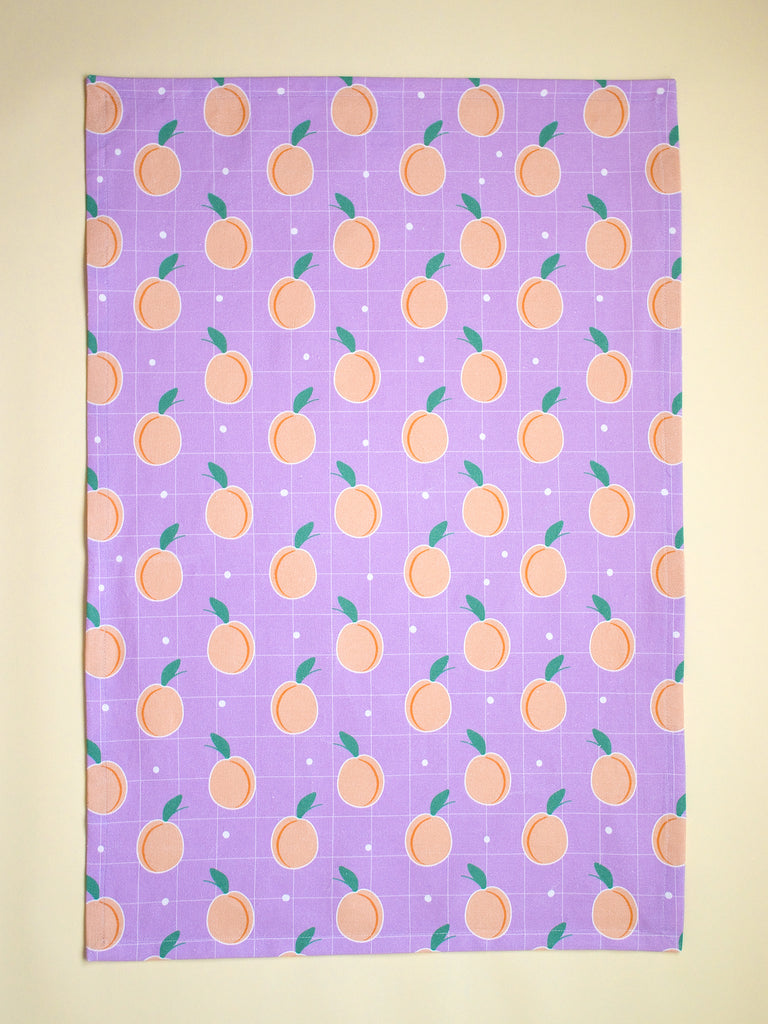 a lilac tea towel with a fun peaches repeating pattern 
