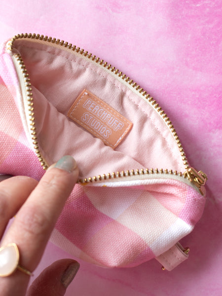 A pink gingham and yellow sunshine-printed coin purse held open by female fingers to show a fabric label reading Peachpuff Studios.