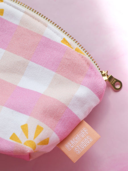 A close-up detail of a zip pouch in a pink gingham printed fabric with a gold metal zipper.