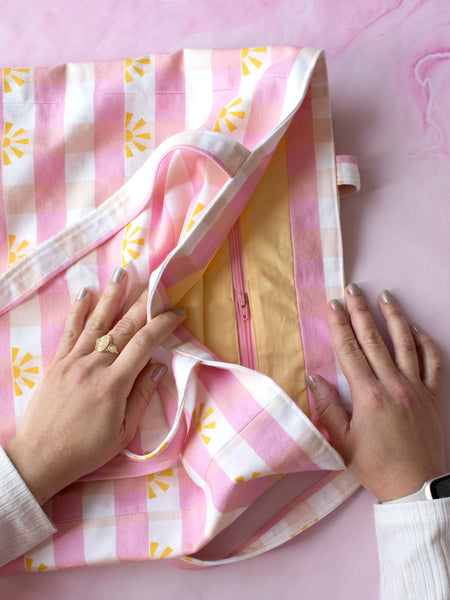 A female hand opens a tote bag to reveal an inside zipper pocket.