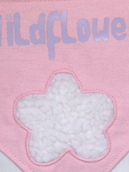 A close-up of a pink canvas banner that reads Wildflower with a fluffy white flower.