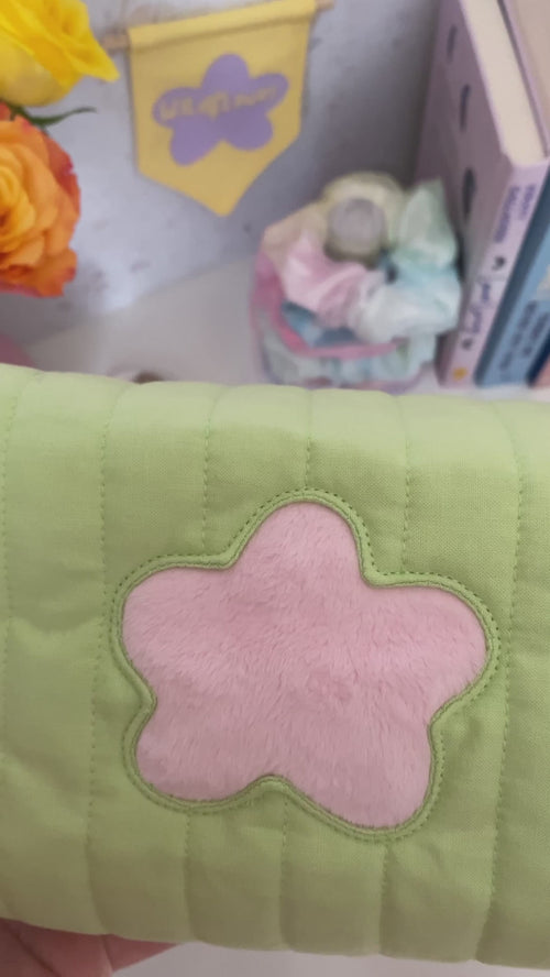 A green quilted zip pouch with a fluffy pink flower in the centre is opened, and the beauty content is emptied on a dressing table.