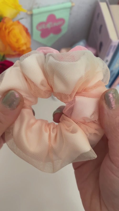 A rainbow scrunchie is shown to the camera while it's stretched open and closed. A female is wearing two scrunchies on her wrist, and she spins them back and forth.