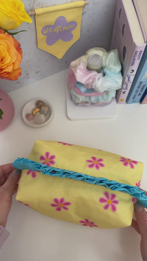 A yellow floral and blue ruffle zip pouch is opened, and the beauty content is emptied on a dressing table.