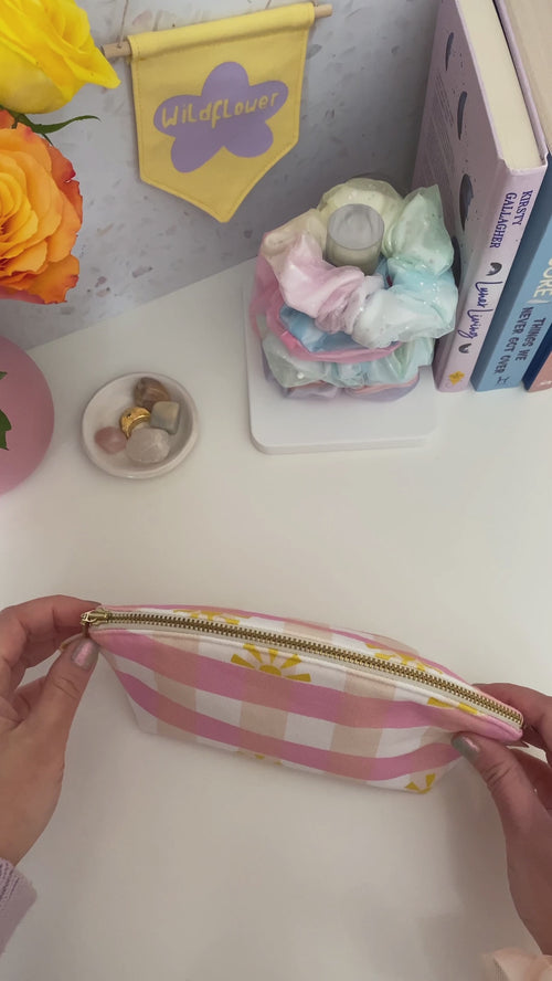 A pink gingham printed zip pouch is opened, and the beauty content is emptied on a dressing table.