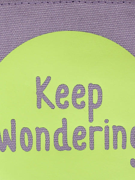 A close-up of a purple canvas banner that reads 'Keep Wondering' in a green circle.