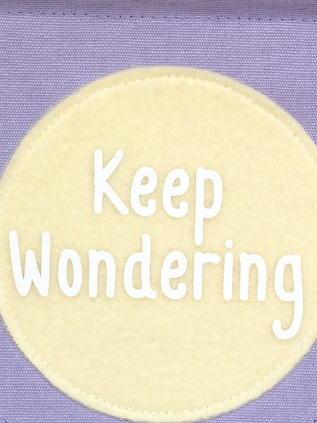 A close-up of a purple canvas banner that reads 'Keep Wondering' in a yellow circle.