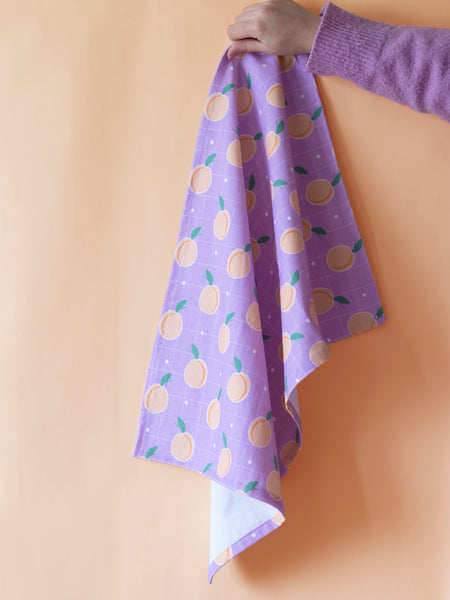 A purple tea towel with peaches held against an orange background