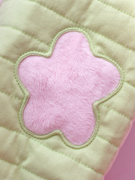 A close-up detail of a green quilted makeup bag with a fluffy pink flower in the centre.