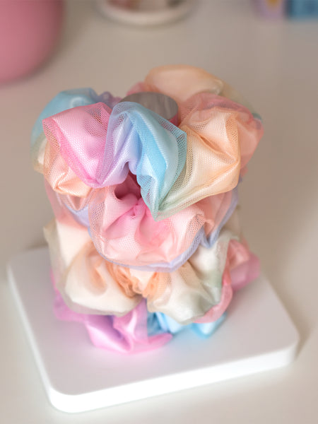 Four rainbow-coloured scrunchies are placed on top of each other on a white and clear holder.