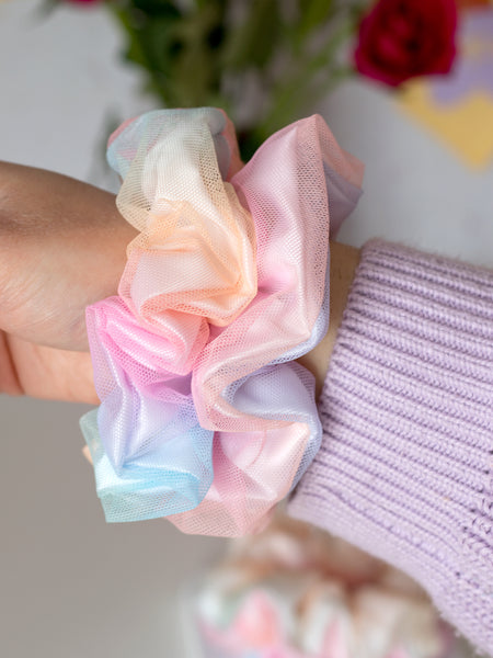 A close-up of two rainbow-coloured scrunchies that are on a female wrist.