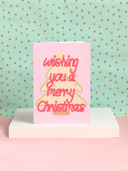 A Christmas card with 'wishing you a merry christmas' in front of a pastel Christmas tree on a white block.