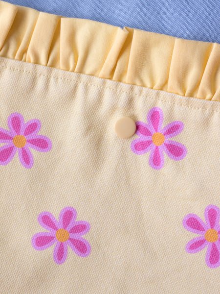 Close-up details of a blue tote bag with a yellow floral front pocket and ruffle.