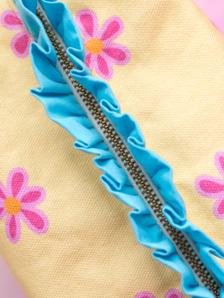 A close-up detail of yellow fabric and pink floral with blue ruffles zip pouch.