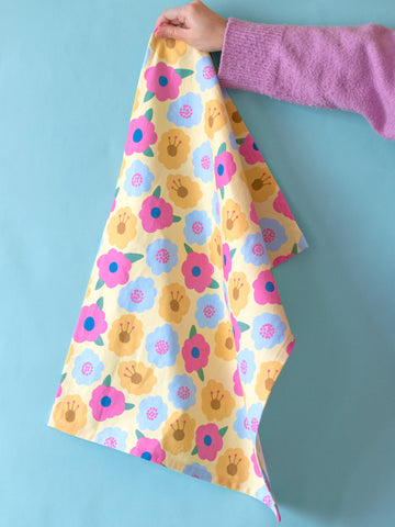 a yellow tea towel held by a pair of hands on a blue background