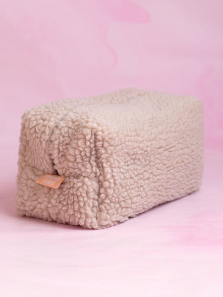 A biscuit-coloured teddy makeup bag on a pink marbled foreground.