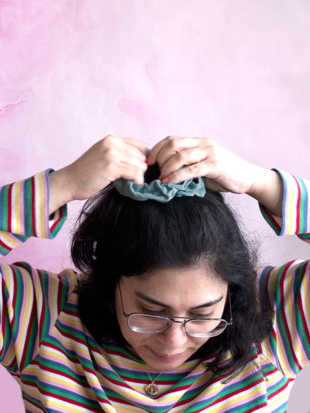 A female tying a blue corduroy scrunchie around the top of her hair. 