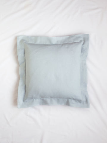 A light blue cotton linen cushion on the centre of a white bedsheet.