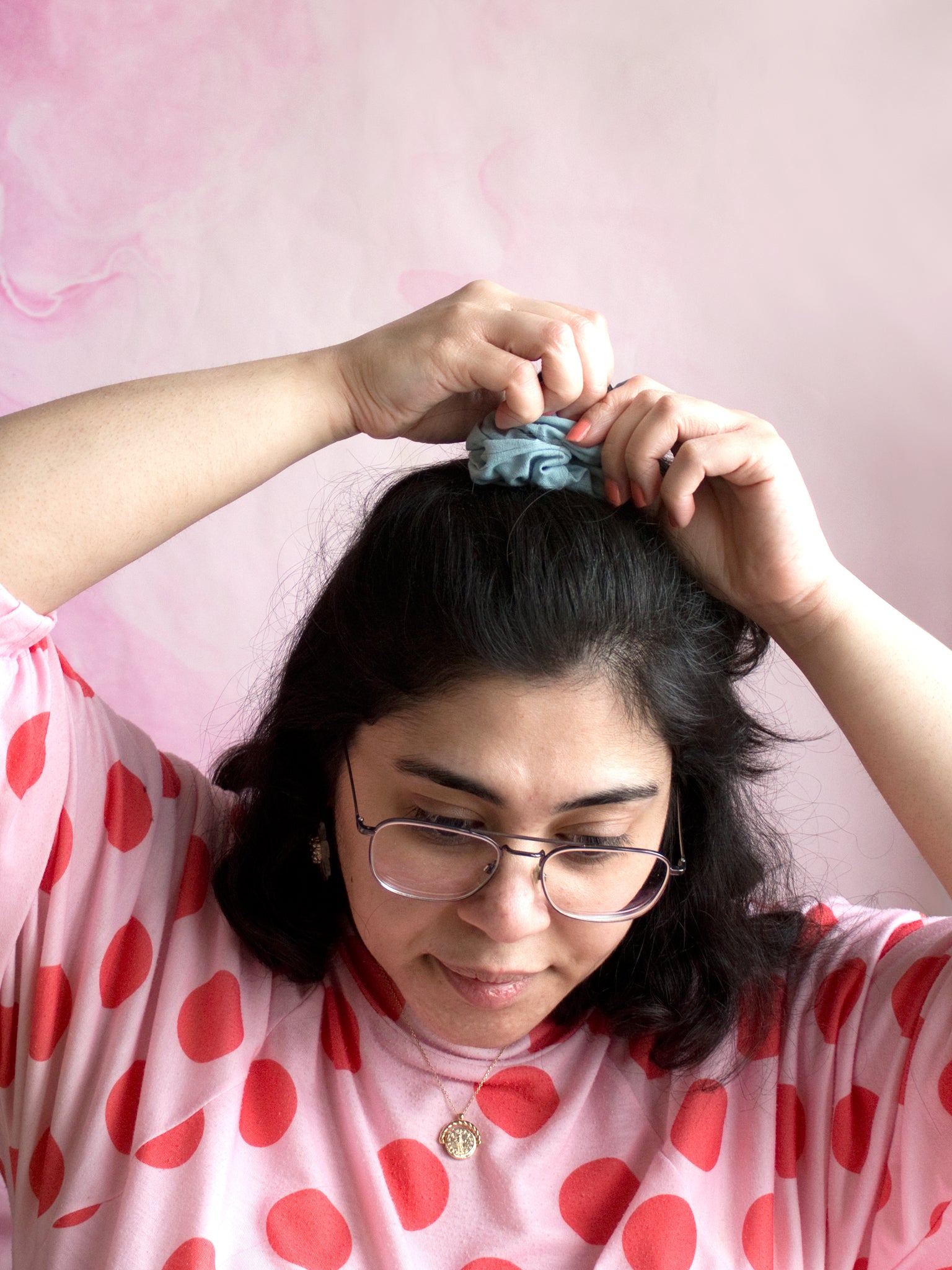A female tying a blue linen scrunchie around the top of her hair. 