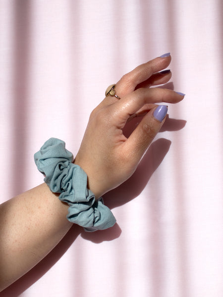A blue linen scrunchie on a female wrist, who is wearing a ring and purple nail varnish.
