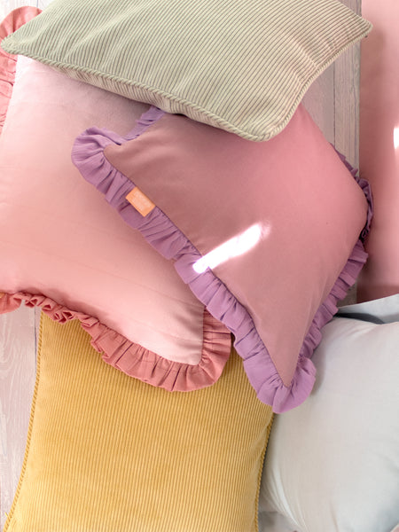 Five different colourful cushions sporadically placed on a white wooden floor laying on top of each other.